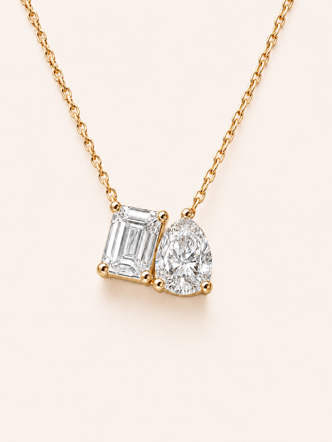 An emerald and pear cut two-stone pendant necklace in 14K gold